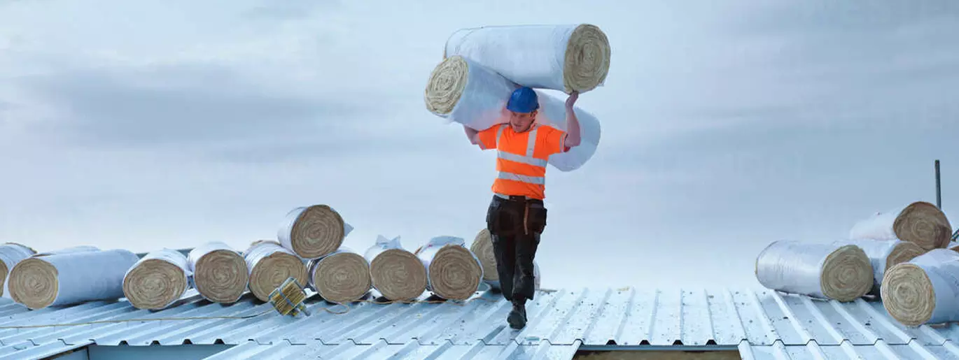 Asentaja kantaa eristerullia tehtaan katolla.
